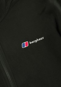 Svart fleecejakke med glidelås, med en liten brodert logo i rødt og blått på venstre brystområde. Myk tekstur og glatt overflate.