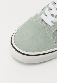 Sneaker in suede verde chiaro con lacci bianchi, rifiniture nere e suola in gomma testurizzata. Punta arrotondata e dettagli di cucitura discreti.