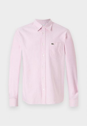 Košulja dugih rukava u ružičastim i bijelim vertikalnim prugama. Ima ovratnik, gumbe sprijeda i mali zeleni logo na džepu na grudima.