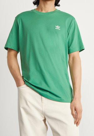Zelené bavlněné tričko s kulatým výstřihem, krátkými rukávy a malým bílým logem Adidas na levé části hrudi. Hladká textura.
