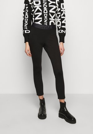 Person iført sorte tætsiddende bukser med elastisk DKNY taljebånd, sorte ankelstøvler og en sort-hvid DKNY logo trøje.