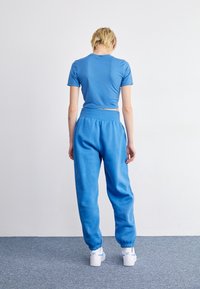 Blå kortärmad t-shirt och blå sweatpants, båda i ett mjukt material. Byxorna har resårmidja och mudd. Vita sneakers är på.