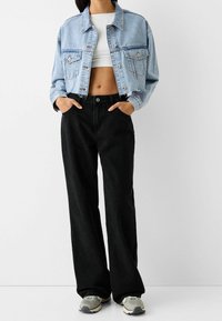 Light blue denim cropped jacket with two front pockets, paired with high-waisted black wide-leg pants. Gray and white sneakers complete the look.