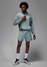 Šviesiai žalia džemperio su kengūros kišene komplektacija, derinama su atitinkamomis šortais. Apranga pasižymi lygiu paviršiumi ir sportiniais batais su raštuotu dizainu.