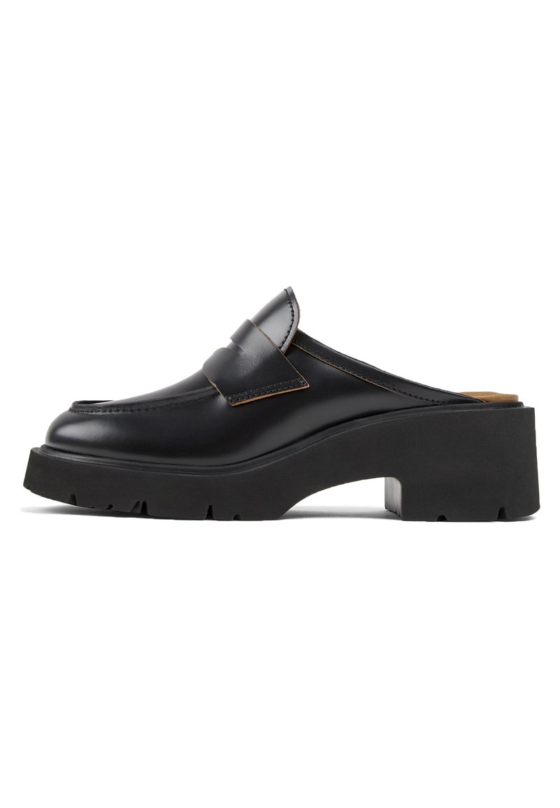 Scarpa slip-on in pelle nera con suola platform in gomma nera chunky e dettagli cuciti sulla parte superiore. Presenta una larga fibbia sulla parte anteriore.