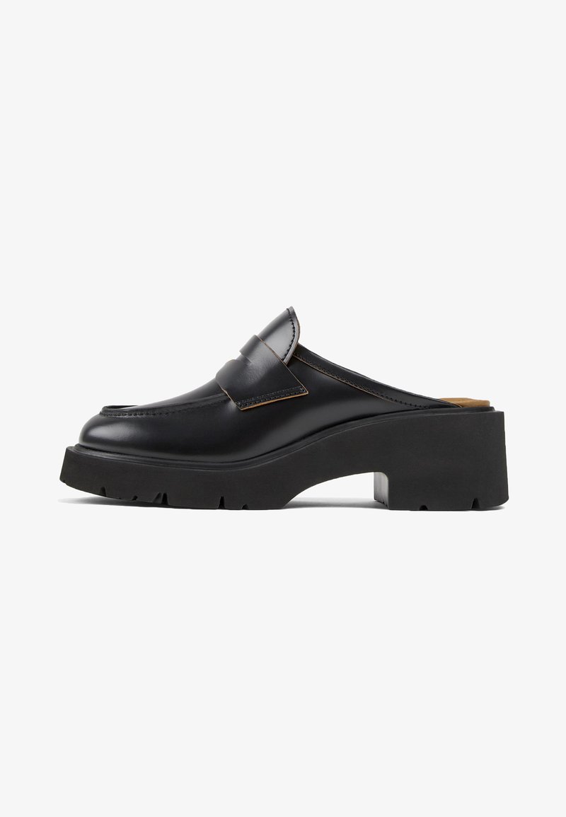 Scarpa slip-on in pelle nera con suola platform in gomma nera chunky e dettagli cuciti sulla parte superiore. Presenta una larga fibbia sulla parte anteriore.