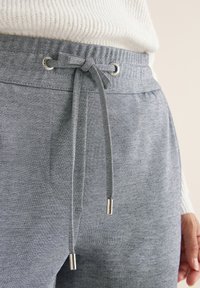 Grijze joggings met een verstelbare tailleband, met een gladde textuur, zilveren uiteinden van de koord en zijzakken. Zacht materiaal is duidelijk aanwezig.