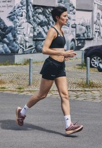 Zwarte sportbeha, zwarte hardloopshorts en roze hardloopschoenen met witte sokken. Hardlopen op een geplaveide straat met een muurschildering op de achtergrond.