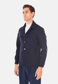 Giacca di lana blu navy con chiusura a bottoni, due tasche nel petto e collo. Caratterizzata da una vestibilità strutturata e una texture liscia.