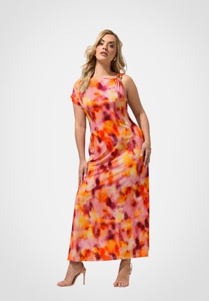 Frau posiert in einem lebhaften orange-, pink- und gelbfarbenen abstrakten Print ärmellosen Maxikleid und nudefarbenen High-Heel-Sandalen vor weißem Hintergrund.