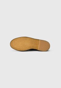 Semelle de chaussure avec une surface en caoutchouc crépe lisse et brun clair et une section de talon texturée sur un fond blanc uni.