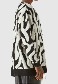 Översize tröja i stickad tyg med ett svart och vitt abstrakt mönster, rund halsringning samt ribbade muddar och fåll.