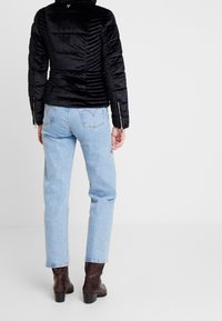 Veste à coussin en velours noir avec des côtes horizontales, assortie à un jean droit bleu clair et des bottes à talons brunes.