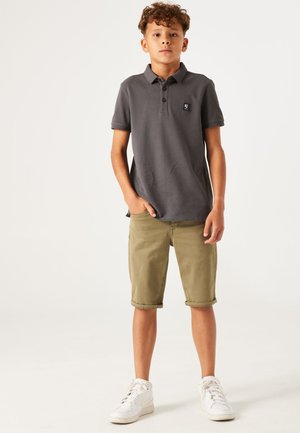Polo gris à manches courtes, avec trois boutons et une broderie de logo. Shorts olive à mi-cuisses, avec les ourlets retroussés, assortis à des baskets blanches.