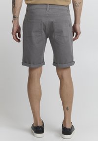 Gray denim shorts with rolled cuffs, featuring back pockets and subtle stitching details. Worn with black sneakers on bare legs.