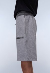 Gray cotton shorts with a drawstring waist, side pockets, and a black logo detail on the left thigh. Smooth texture, knee-length design.
