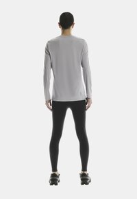Ljusgrå långärmad tr�öja med rund hals, kombinerad med svarta leggings och svarta träningsskor. Slät, åtsittande design med minimal varumärkning.