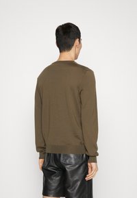 Brauner Strickpullover mit langen Ärmeln und rundem Ausschnitt, der eine glatte Textur und einen gerippten Saum aufweist, kombiniert mit schwarzen Leder-Shorts.