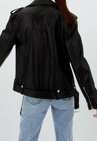 Czarna skórzana kurtka motocyklowa z naramiennikami, rękawami na zamek i srebrnymi detalami, w połączeniu z jasnoniebieskimi dżinsami.