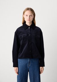 Veste-chemise en velours côtelé bleu foncé avec un col pointu, fermeture à boutons à l'avant et deux poches poitrine. Présente des manches longues et une coupe décontractée.