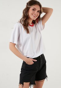 Biela bavlnená tričko s krátkymi rukávmi v kombinácii s čiernymi riflovými šortkami s rozstrapkanými okrajmi. Outfit je doplnený červeným náhrdelníkom.