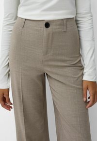 Světle hnědé široké kalhoty s jemnou texturou, se zapínáním na jeden knoflík, poutky na opasek a předními kapsami.