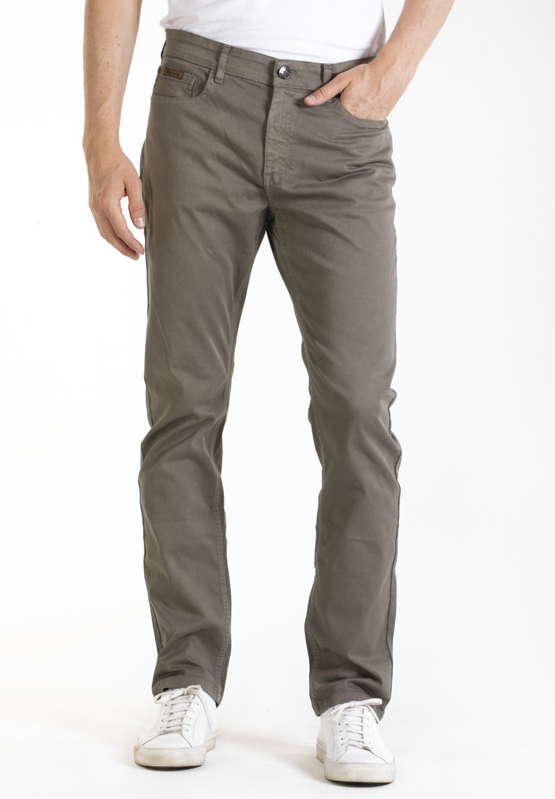 Chinos légers, de couleur vert olive, avec une coupe droite, dotés d'une fermeture éclair, d'un bouton et de poches avant. Portés avec des baskets blanches.