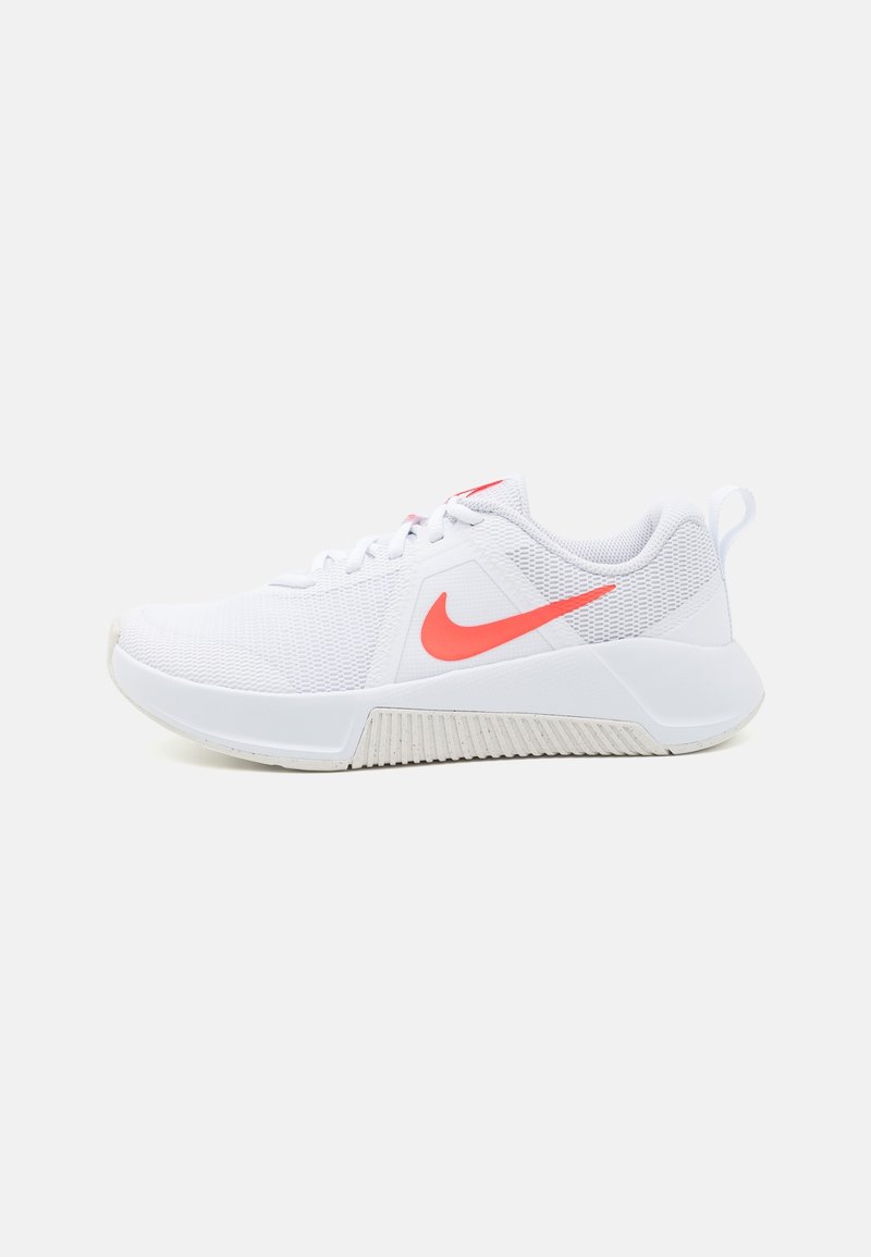 Zapato deportivo blanco con parte superior de malla, que presenta un brillante swoosh de Nike en color naranja, suela texturizada y cuello acolchado para mayor comodidad.