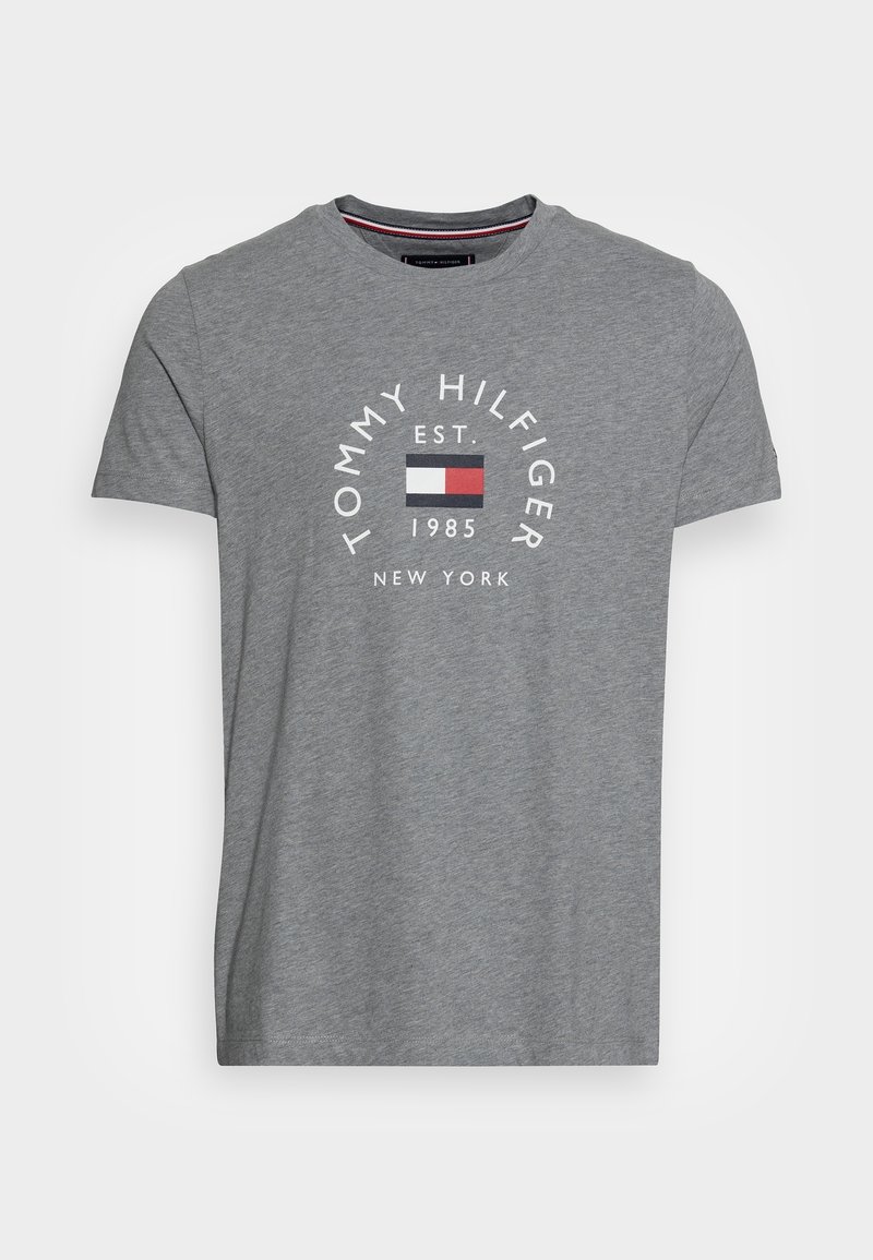 Camiseta de algodón gris con cuello redondo, mangas cortas y un gráfico en la parte frontal que dice "TOMMY HILFIGER EST. 1985" y un logo en bloques de color.