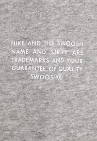 Grått tyg med vit text som säger "Nike och Swoosh-namnet och -stripen är varumärken och din garanti för kvalitet Swoosh®."