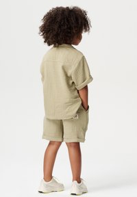 Chemise courte à manches courtes vert clair et shorts assortis, en tissu texturé avec des manches roulées, associés à des baskets claires avec des accents jaunes.