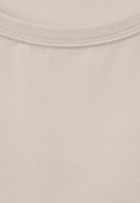 Ljust beige bomullstyg med en slät textur, med rund hals och en enkel, odekorerad design. Diskreta sömmar synliga.