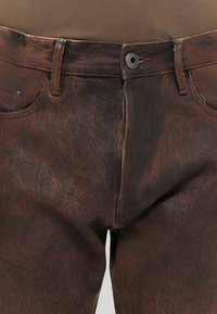 Brune denimjeans med teksturert overflate, med tradisjonell fem-lomme-design og kontraststing. Metallknapplukking inkludert.