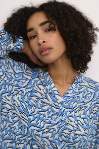 Blusa azul con un patrón de hojas en blanco y negro, con un frente abotonado y una tela suave y texturizada. Diseño con cuello y mangas largas.
