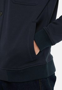 Navy Sweatshirt aus weichem Stoff, ausgestattet mit einem Stehkragen, gerippten Bündchen und einer Fronttasche mit Knopfverschluss.