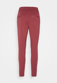 Leggings rouges extensibles avec une taille élastique, coupe ajustée, poches latérales et texture lisse. Le design présente un style de jambe fuselée.