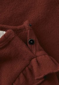 Maroon villa kangas, jolla on röyhelöreuna. Sisältää mustan napin sauman lähellä. Pehmeä rakenne, jossa on kevyt kiilto.