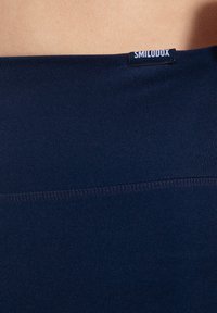 Leggings blu navy senza cuciture con una texture liscia e vita elastica, caratterizzati da un piccolo etichetta nera con testo bianco nella parte superiore.