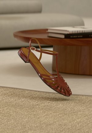 Κόκκινο πέδιλο με λουριά, με υφή και ανοιχτή μύτη, διαθέτει λεπτό λουράκι στον αστράγαλο και χαμηλό τακούνι.