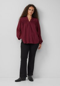 Bordeaux blouse met lange mouwen en een V-hals, met details van verwerkt materiaal, gecombineerd met zwarte rechte broek en zwarte enkellaarsjes.