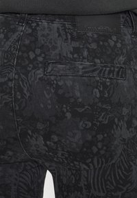 Gros plan sur un pantalon noir à motifs avec une poche arrière et une étiquette de marque en cuir cousue au-dessus de la poche.