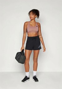 Conjunto atlético com um top de desporto rosa claro e calções pretos com uma cintura elástica, combinado com ténis pretos e uma mala de ginásio preta.