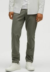 Olive zielenone, lekkie, zwężane spodnie o gładkiej fakturze i elastycznym pasie. Połączone z białymi trampkami i koszulą na guziki.