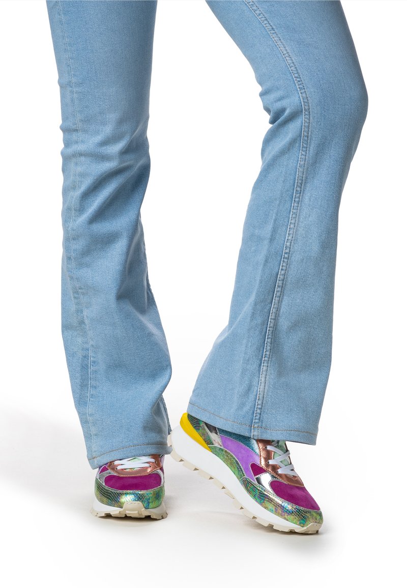 Flerfärgade plattformssneakers med en mix av texturer, inklusive metalliska accenter, lila, gröna och gula detaljer, kombinerat med ljusblå flarejeans.