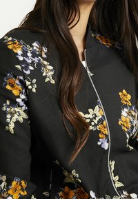 Floral bomber jacket featuring a black fabric with colorful orange, purple, and white flower patterns; silver zipper detail at the front.