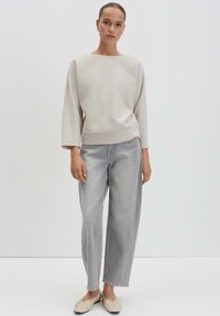 Maglione crema con ampio scollo a barca e maniche lunghe, abbinato a jeans grigi chiari larghi e scarpe slip-on beige. Materiali morbidi.