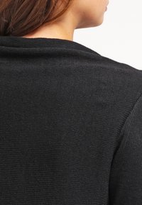 Pull noir texturé vu de dos, mettant en valeur une coupe décontractée et un design simple avec un col lisse.