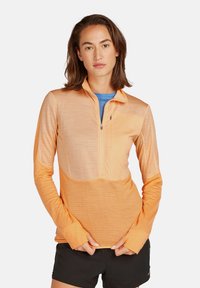 Pomarańczowy pulower z długim rękawem i pół-zamkiem, z teksturowanym wzorem oraz otworami na kciuki w mankietach. Lekki i oddychający materiał.