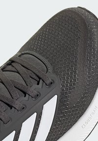 Czarny sportowy but z teksturowaną siateczkową cholewką, wyraźnym systemem sznurowania, gumową podeszwą i białymi paskami na boku.