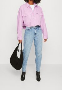 Beskarvad, ljuslila denimjacka med två framfickor, matchad med ljusblå figurnära jeans och en svart texturerad handväska. Spetsiga svarta klackar.